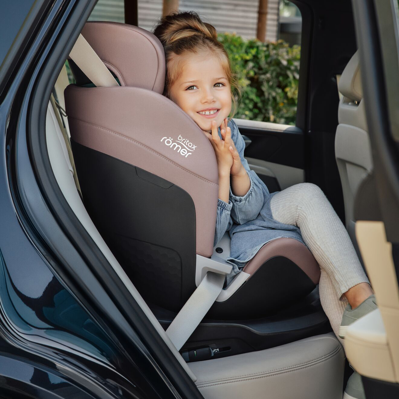 Niña sentada cómodamente en silla de coche Britax Römer Swivel 2 en modo elevador con respaldo, usando cinturón del vehículo